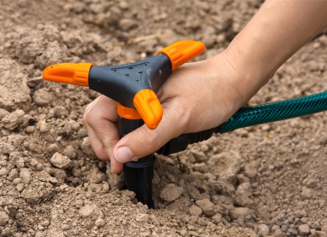 A hand screwing on an orange sprinkler head onto a system.