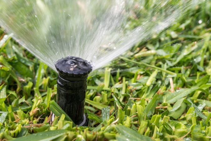 A close-up image of a sprinkler irrigating a lawn.