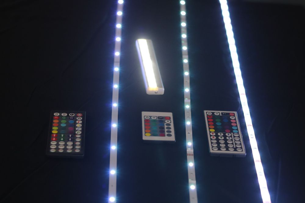 A few of the best LED light strip options glowing brightly in a dark room with their remotes next to them.