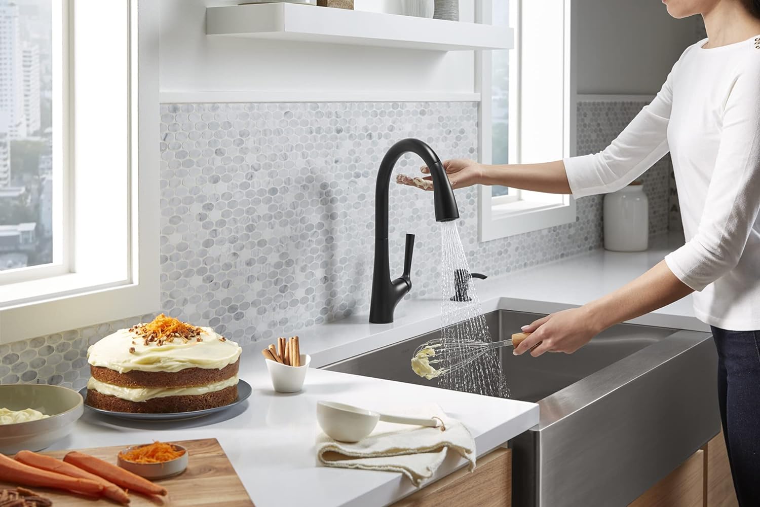 A person using the best touchless kitchen faucet option to clean cake frosting off a wisk.