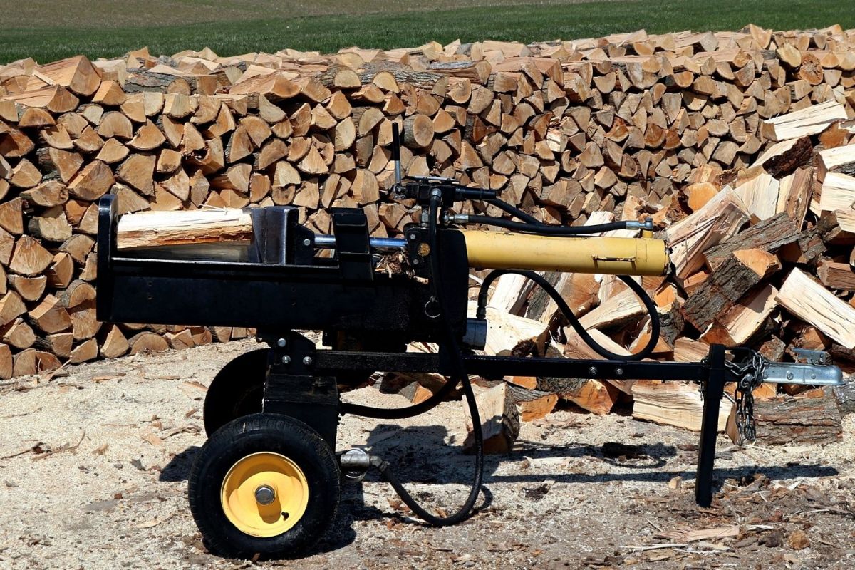 The Best Log Splitter trailer in use splitting firewood with a large stack of split wood in the background.