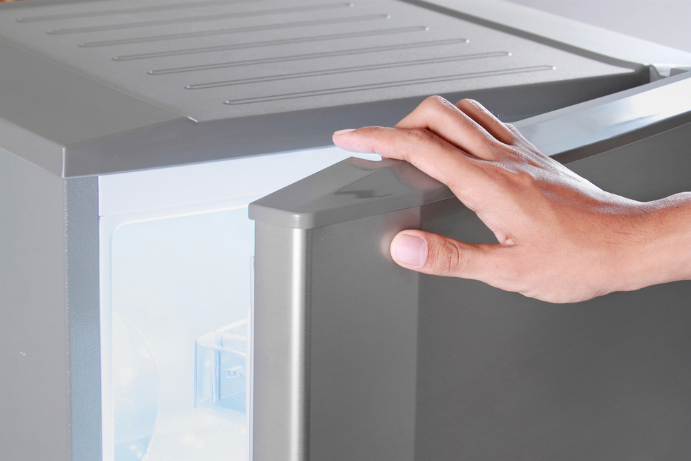 A person's hand opening the best upright freezer using the grip on the top corner.