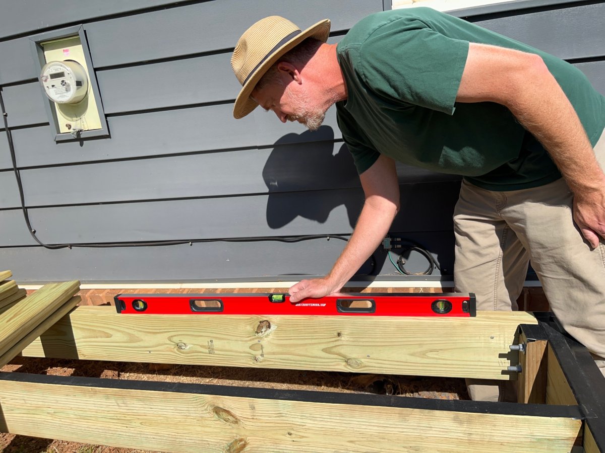 a man in green shirt and hat is using the craftsman box level on a wood deck frame