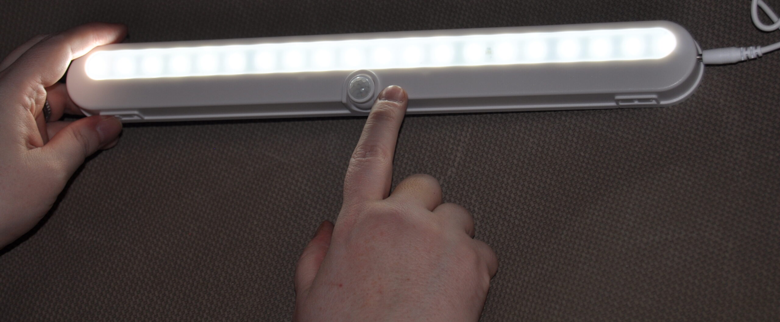 A person's finger next to the on/off button on the best under-cabinet lighting option.