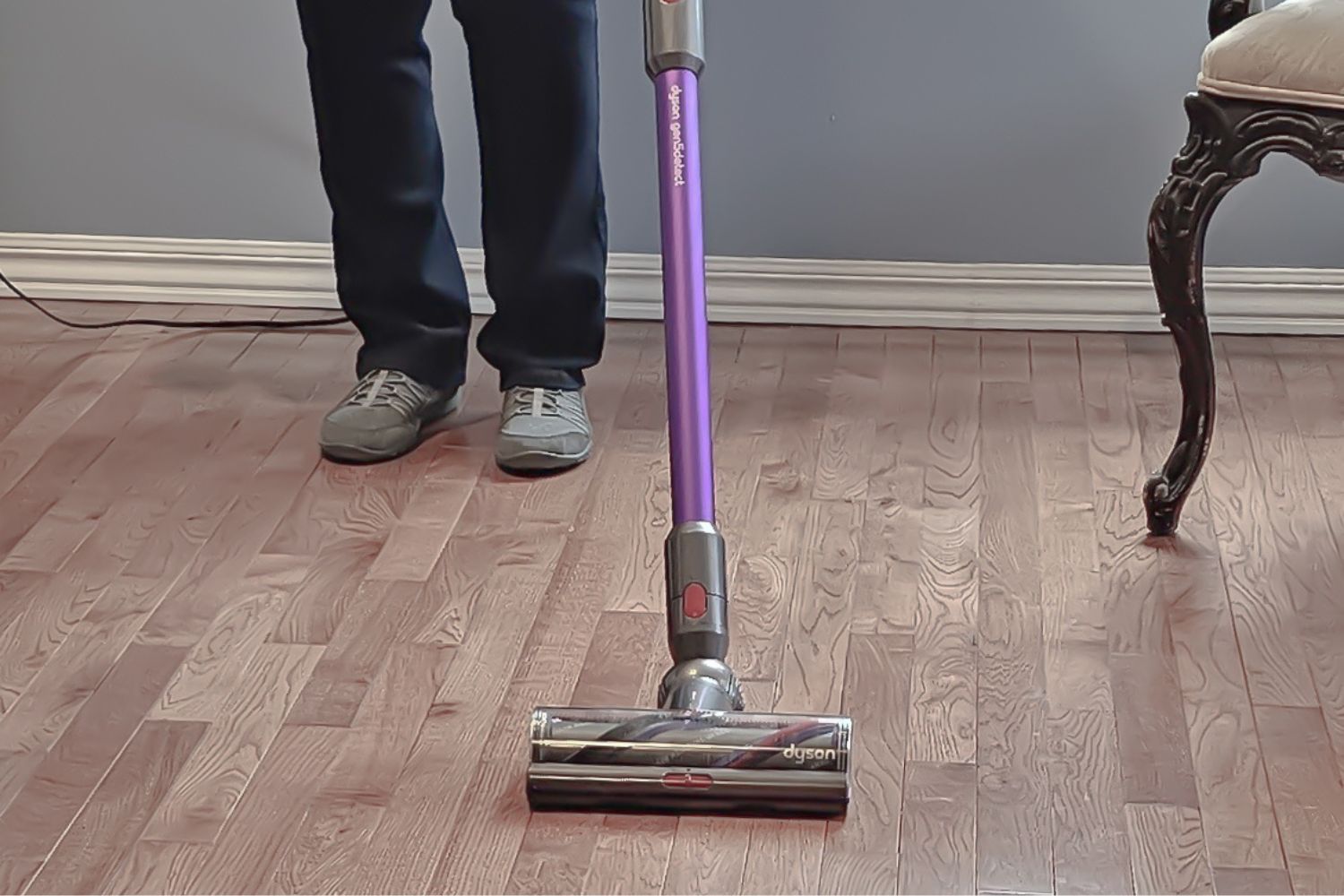 Person cleaning a hardwood floor with purple and silver cordless stick vacuum