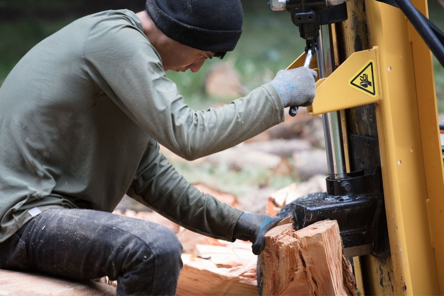 A person wearing gloves and a hat while using the best log splitter to split wood outdoors.