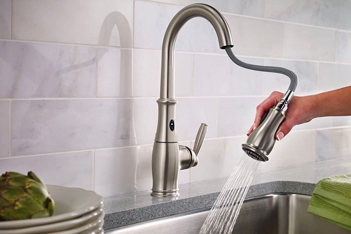 A hand manipulating the sprayer on the best touchless kitchen faucet option to spray out a sink.