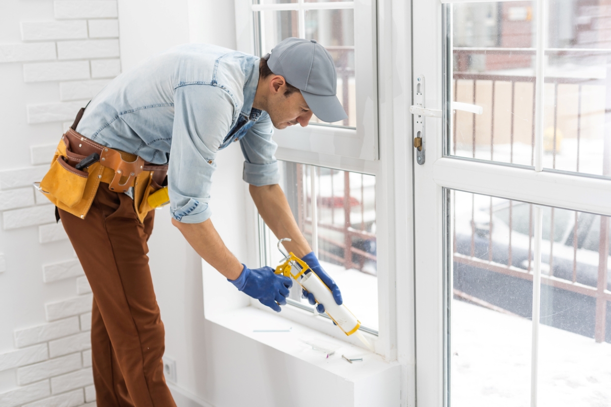 A handyman finishing window install with caulk.