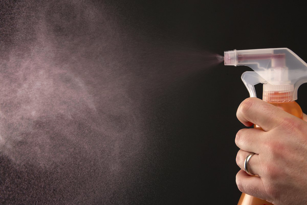 Person puff of spray from non-aerosol spray bottle against a black background.