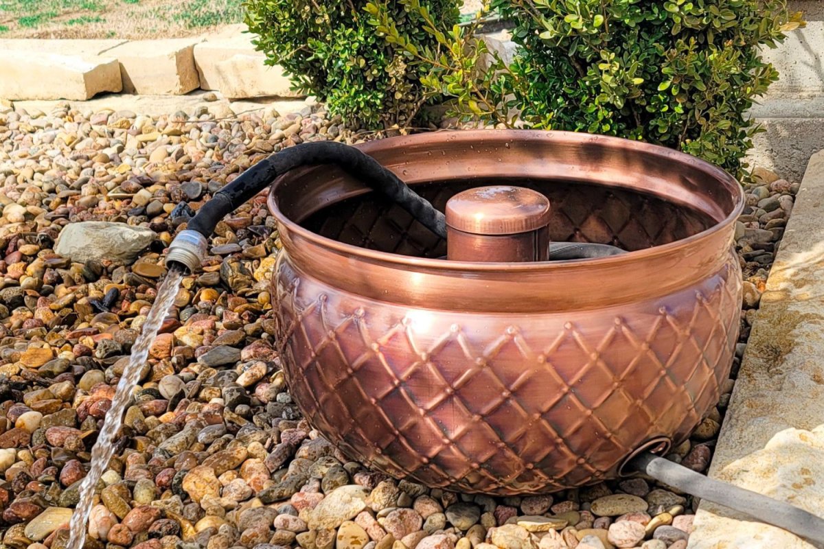 Copper pot hose reel on bed of rocks with black hose spraying water