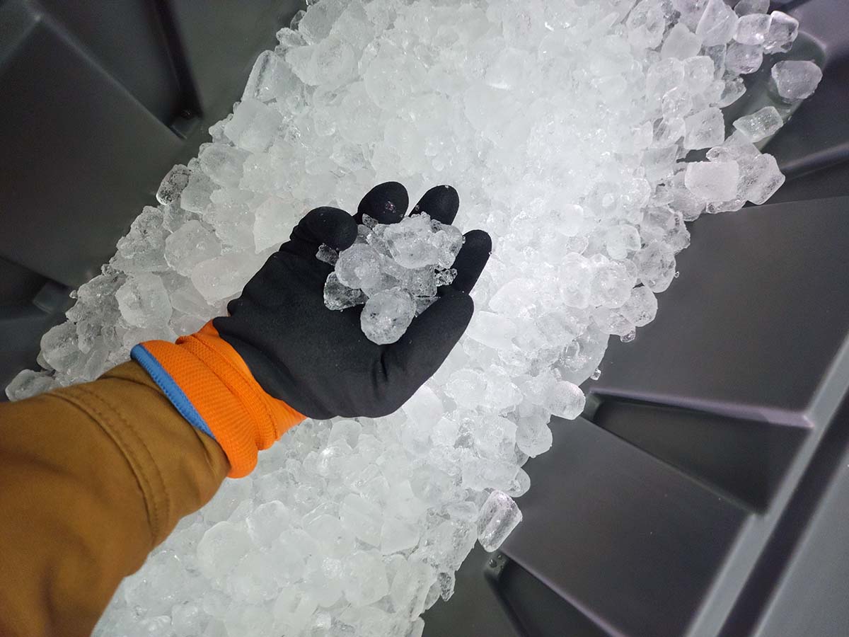 A person getting a handful of ice from a commercial ice maker while wearing the best winter work gloves.