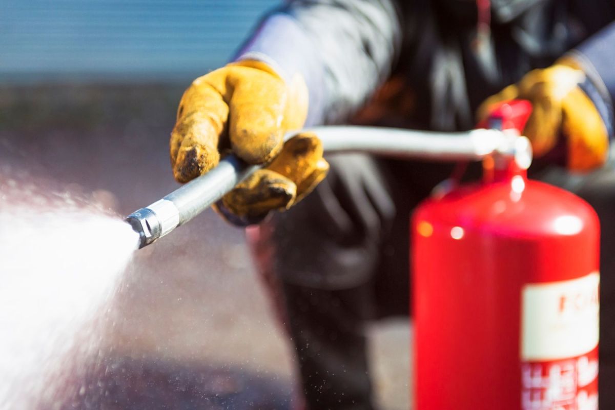 A person wearing work gloves while spraying the best fire extinguisher.