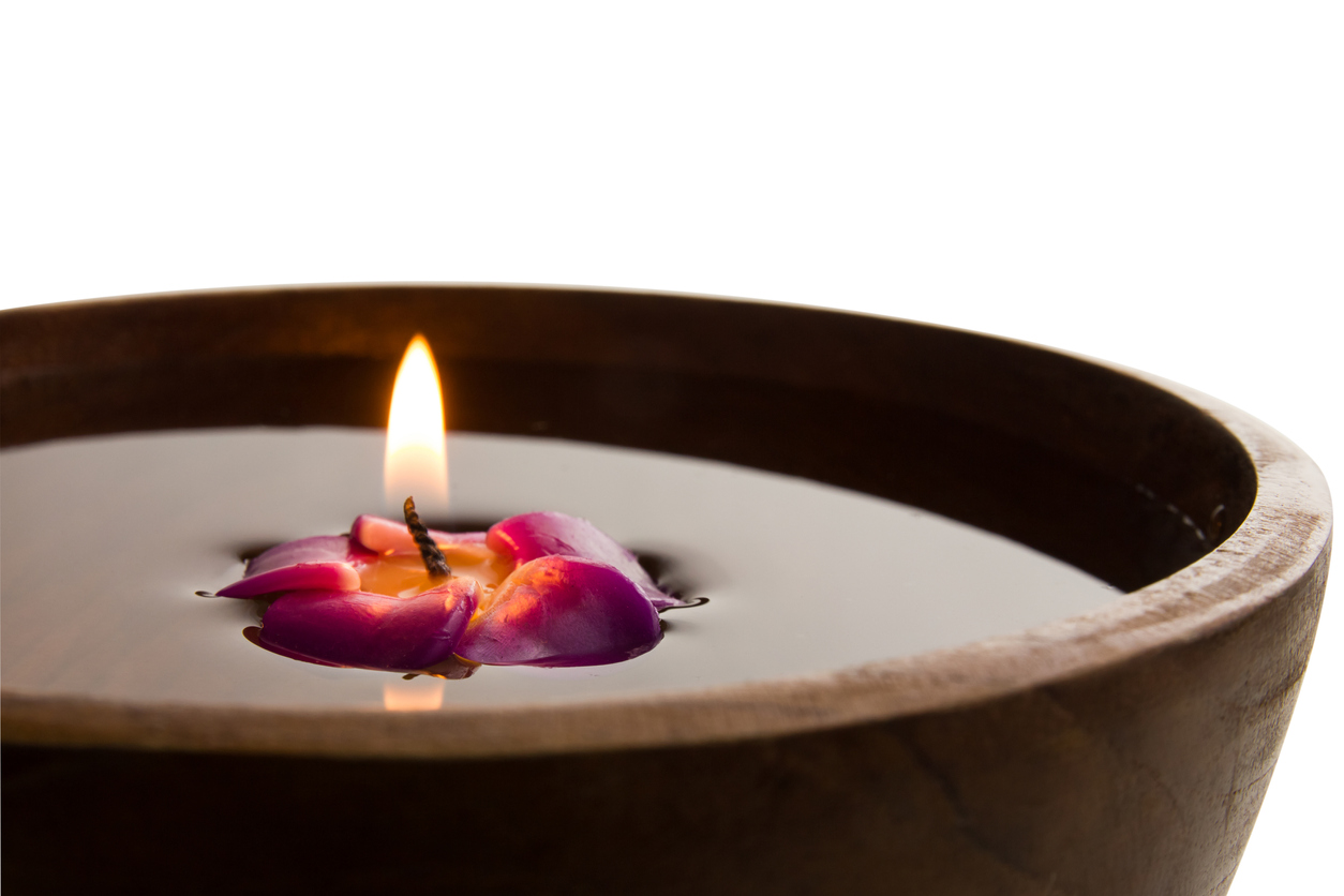 Lit purple candle burned almost to the wick in a small wood bowl filled with water.