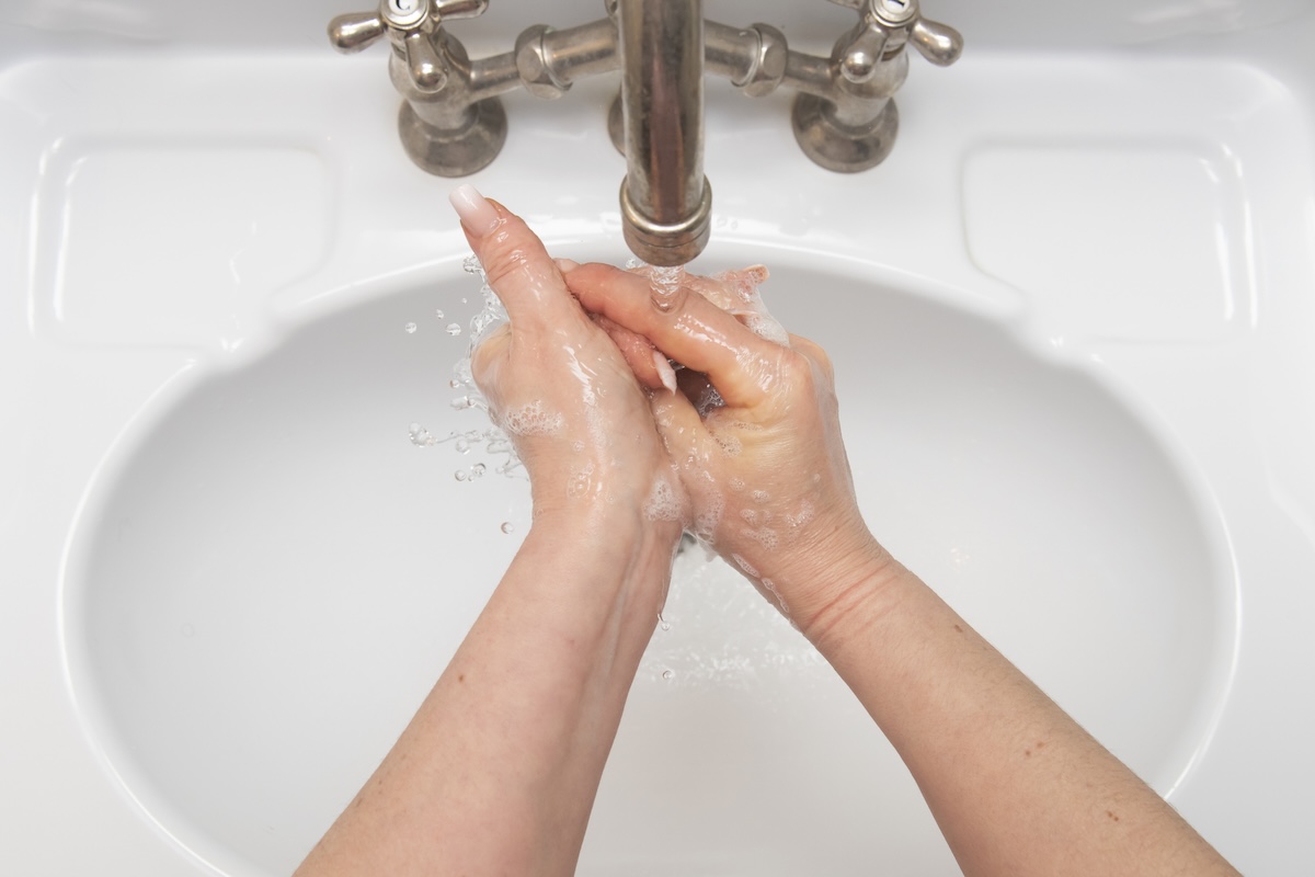 A woman washes her hand under a brushed nickel faucet.
