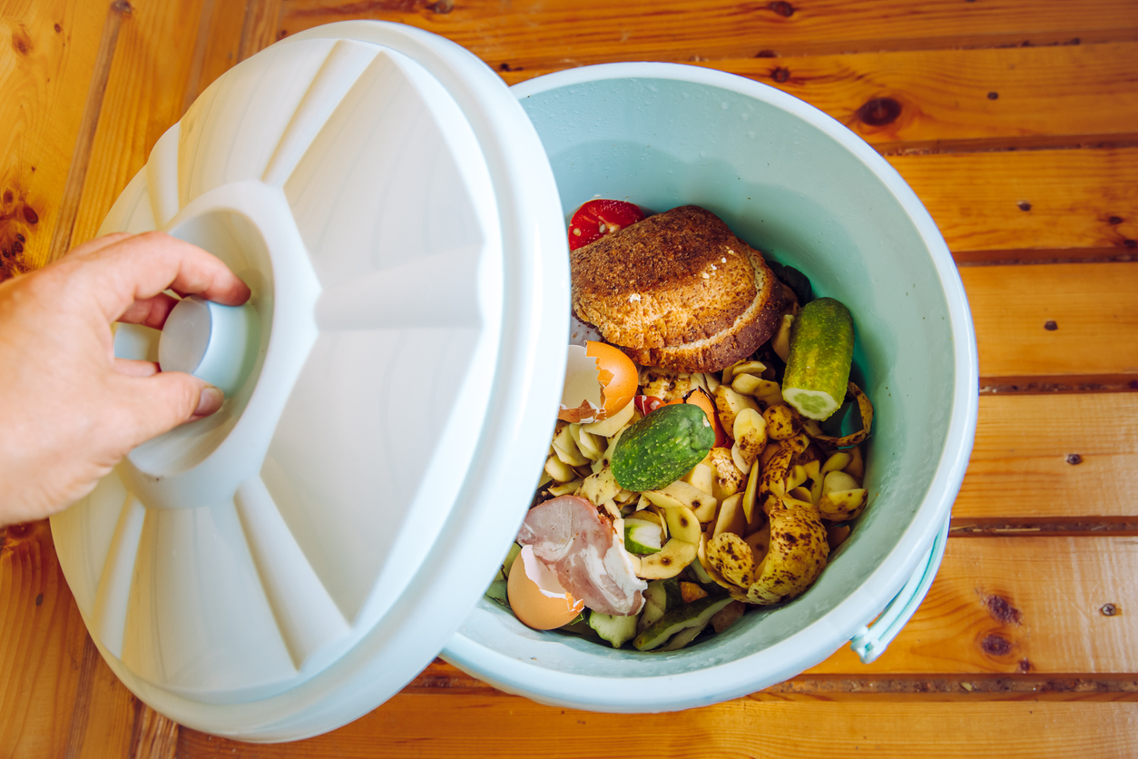 Person putting the lid on a white kitchen compost bin filled with food scraps.