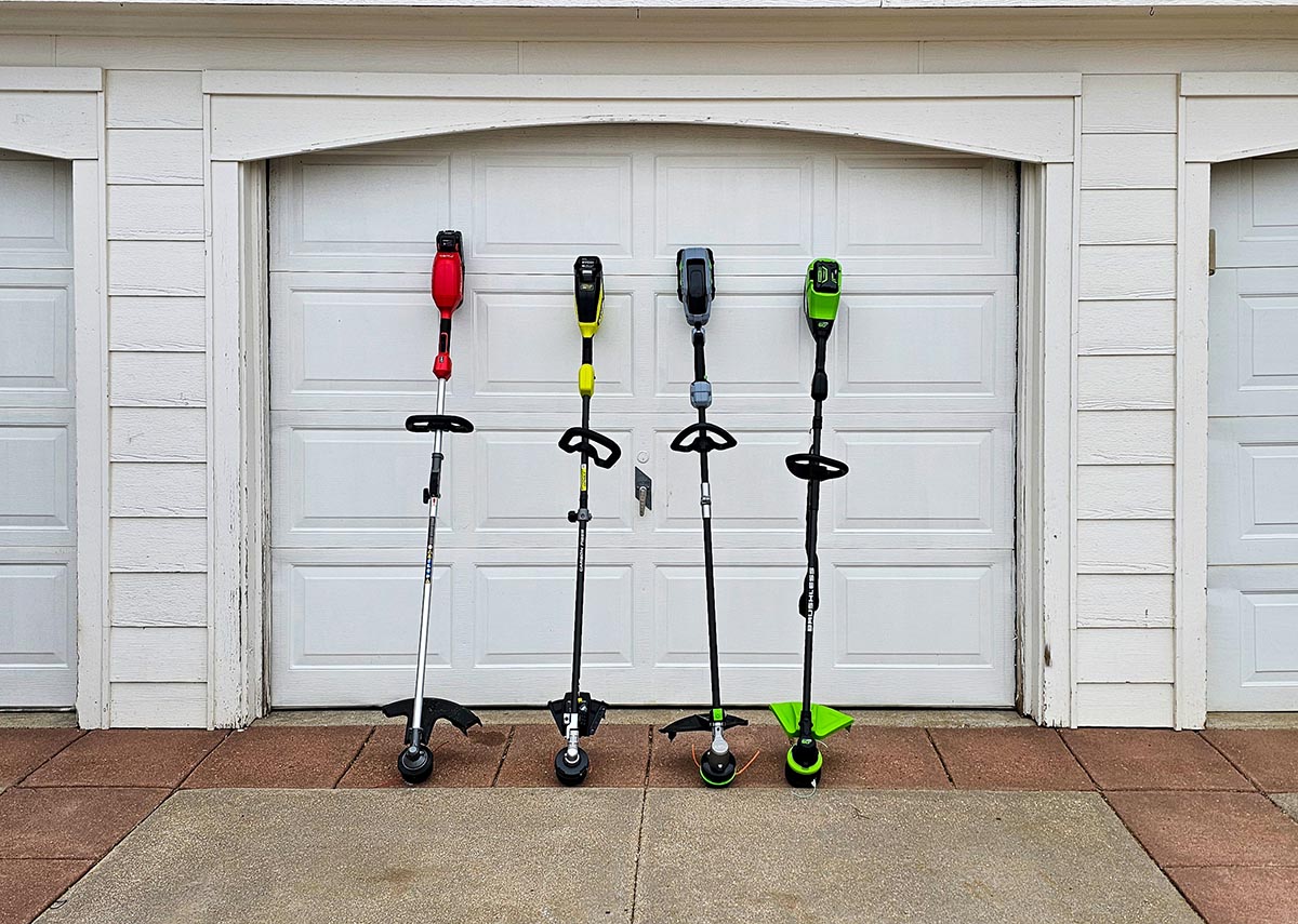 Four of the best battery trimmers leaning against a garage before testing.