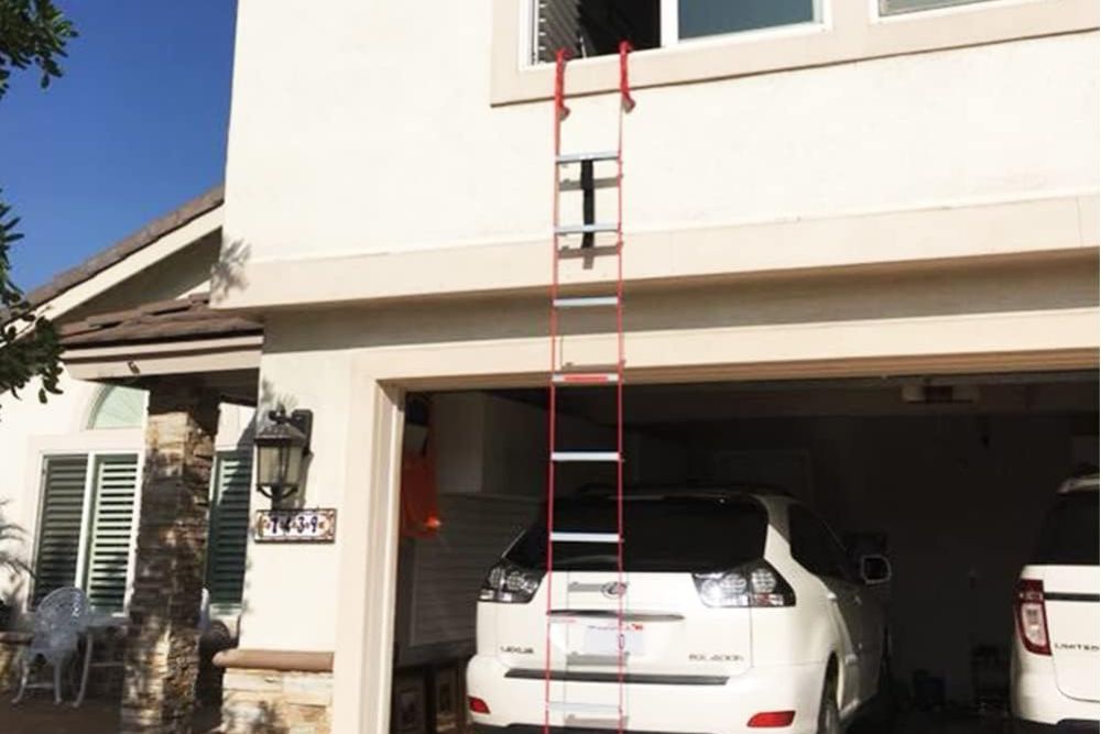 A house with the garage door open and a car inside with a fire escape ladder hanging down from an open window.
