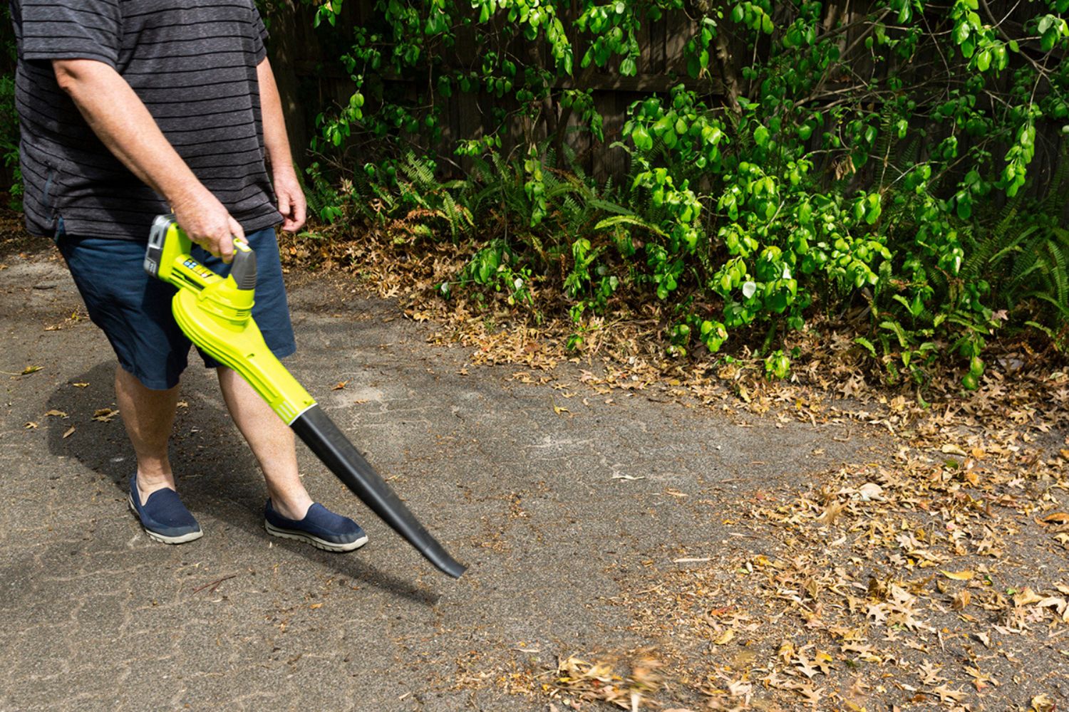 A person using the best battery-powered leaf blower to clear leaves from a wide walkway.