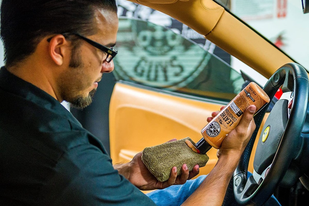 A person putting the best leather cleaner option on a sponge before cleaning a car's leather interior