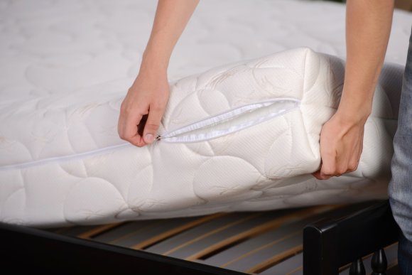 A person zipping one of the best mattress pads closed after putting it on a mattress