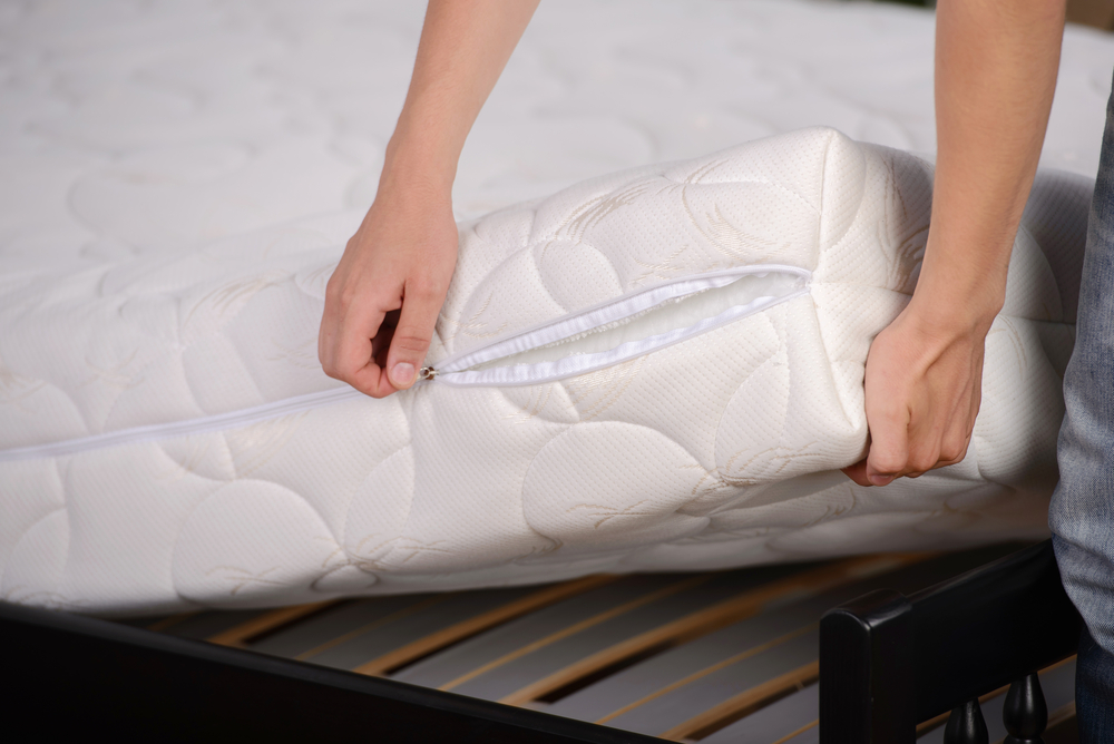 A person zipping the best mattress pad option closed after putting it on a mattress