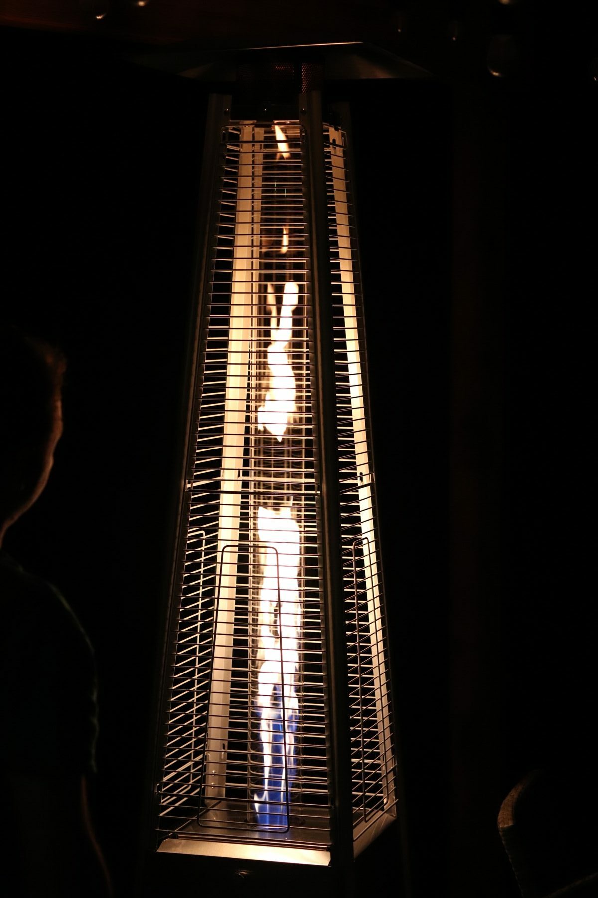Tube-style Tower patio heater in the dark with tall glowing flame