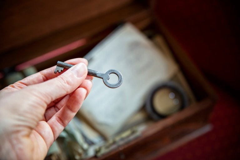 a woman holds an old key in her hand, old wooden box with papers in background.