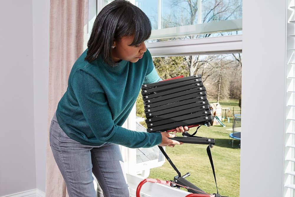A person bending down to insert the best fire escape ladder into an open window.