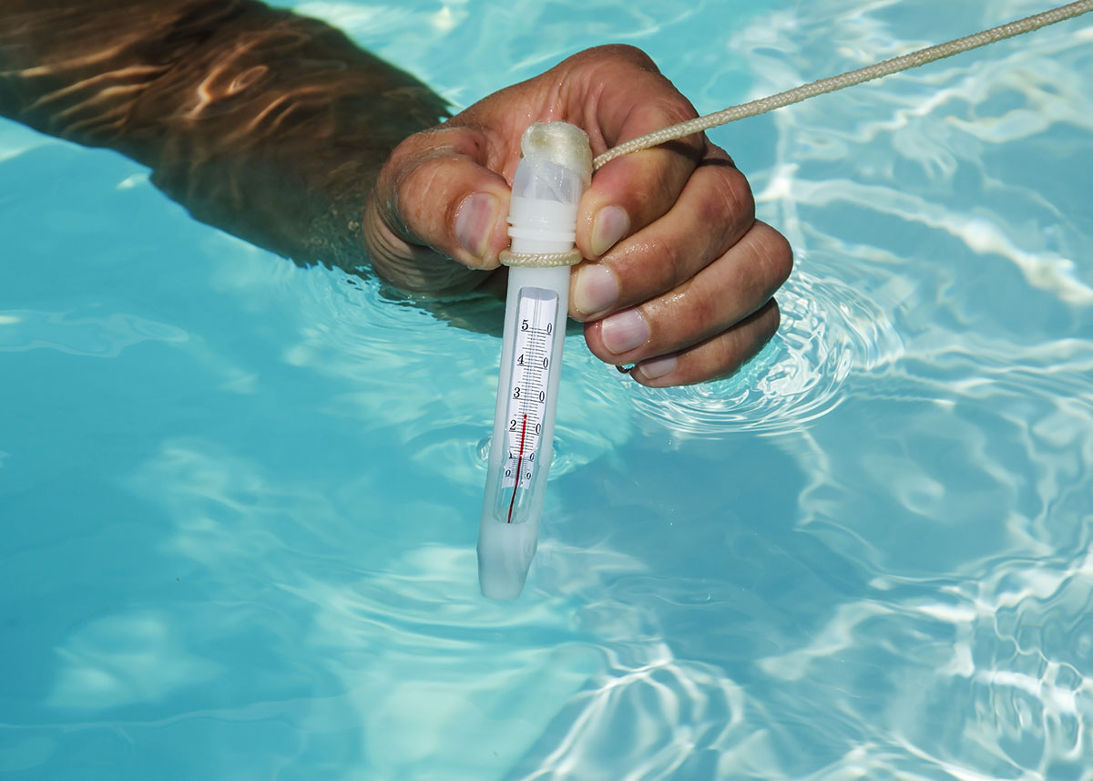 A hand holding a thermometer while in a pool that's being warmed by the best pool heater option