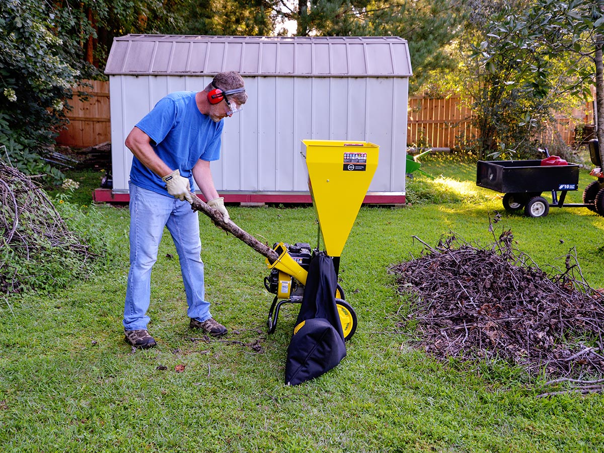 A person feeding a tree branch into the best wood chipper while standing in a yard next to a pile of mulched wood.