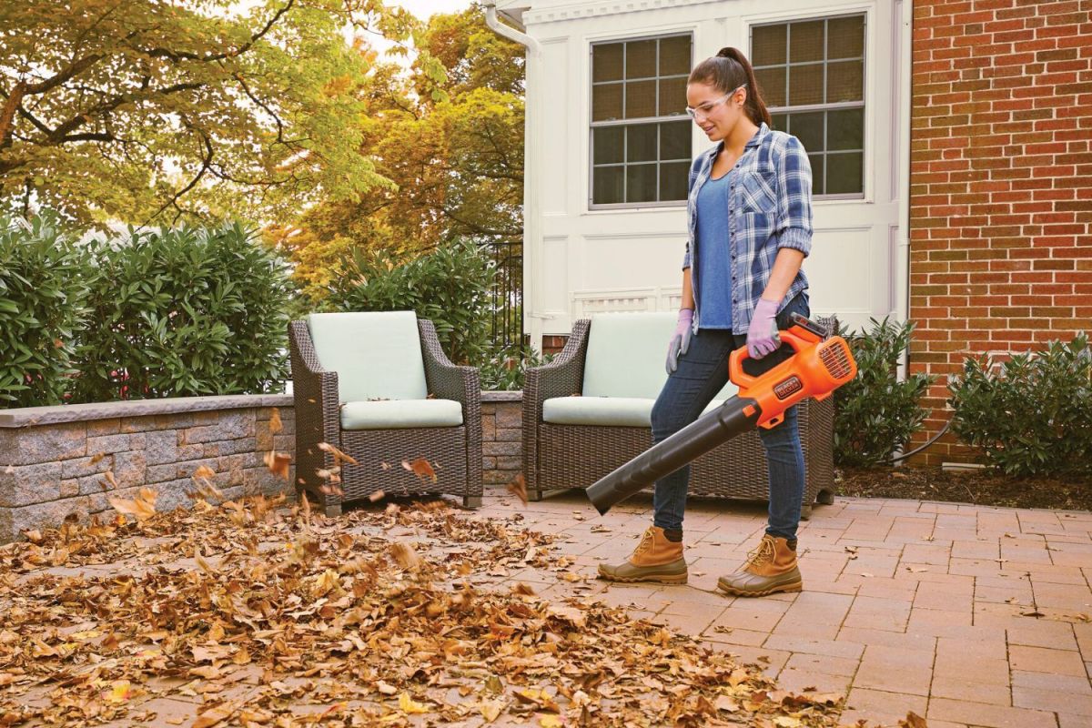 A person using a battery-powered leaf blower to clear leaves from a patio.