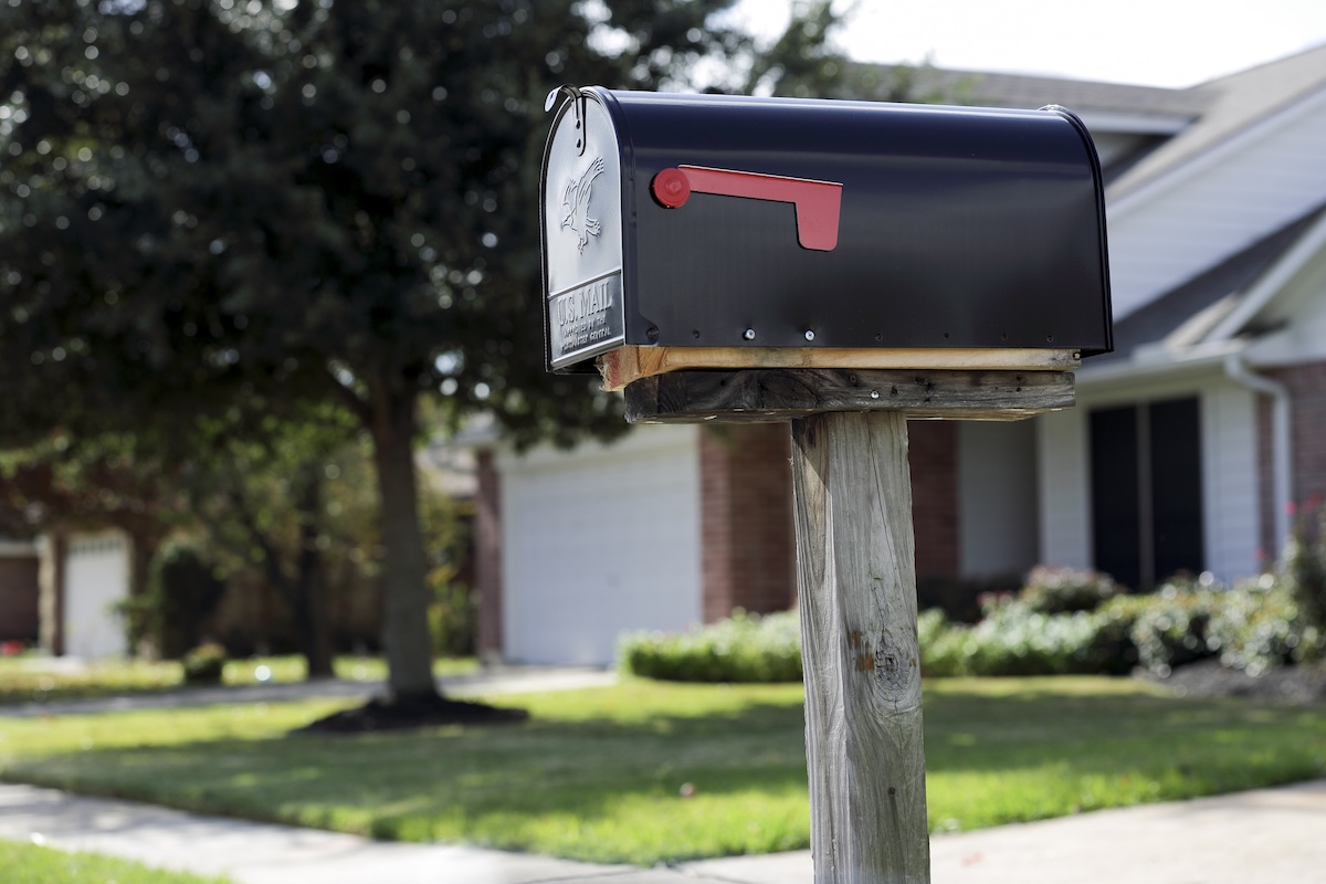 A simple black mailbox stands on the curb outside of a home.