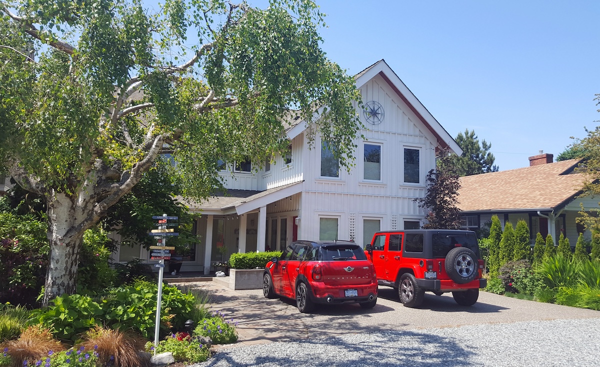Two red cars, a coup and an SUV, parked in front of a large white home.