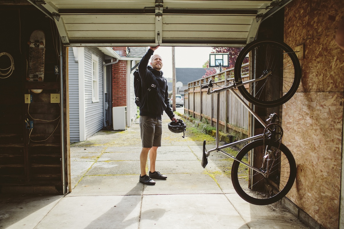 A man closes the door to his garage, which contains a bicycle.