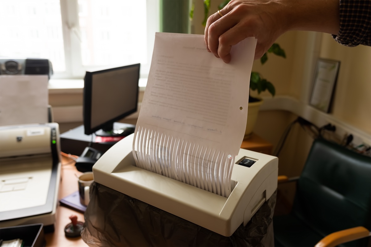 An unidentified hand feeds a document through a paper shredder.