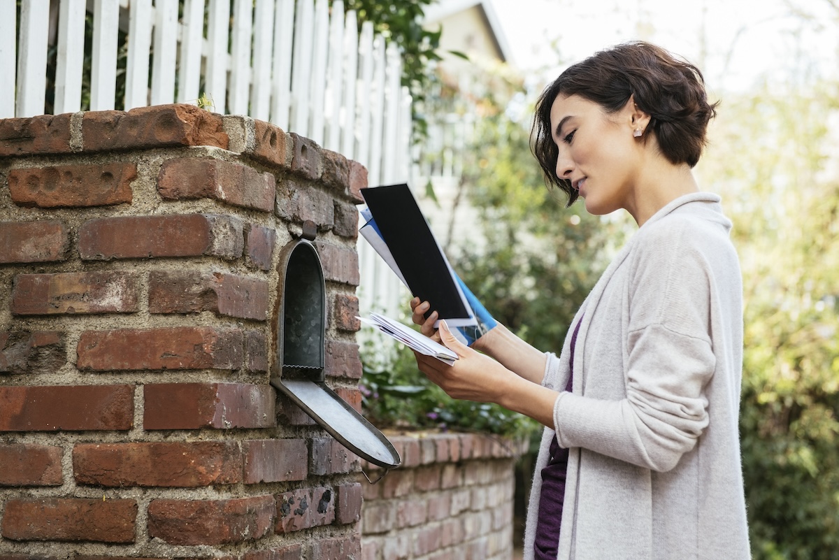 A woman with short hair takes the mail from a mailbox.