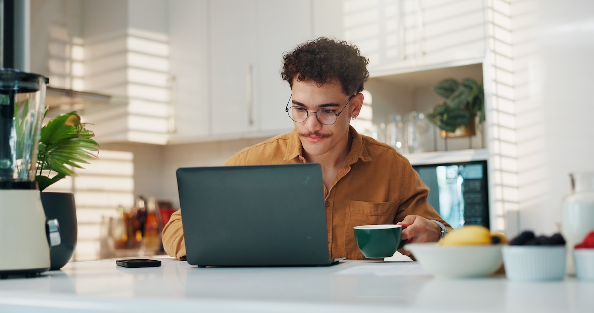 A younger man uses a laptop in his kitchen.