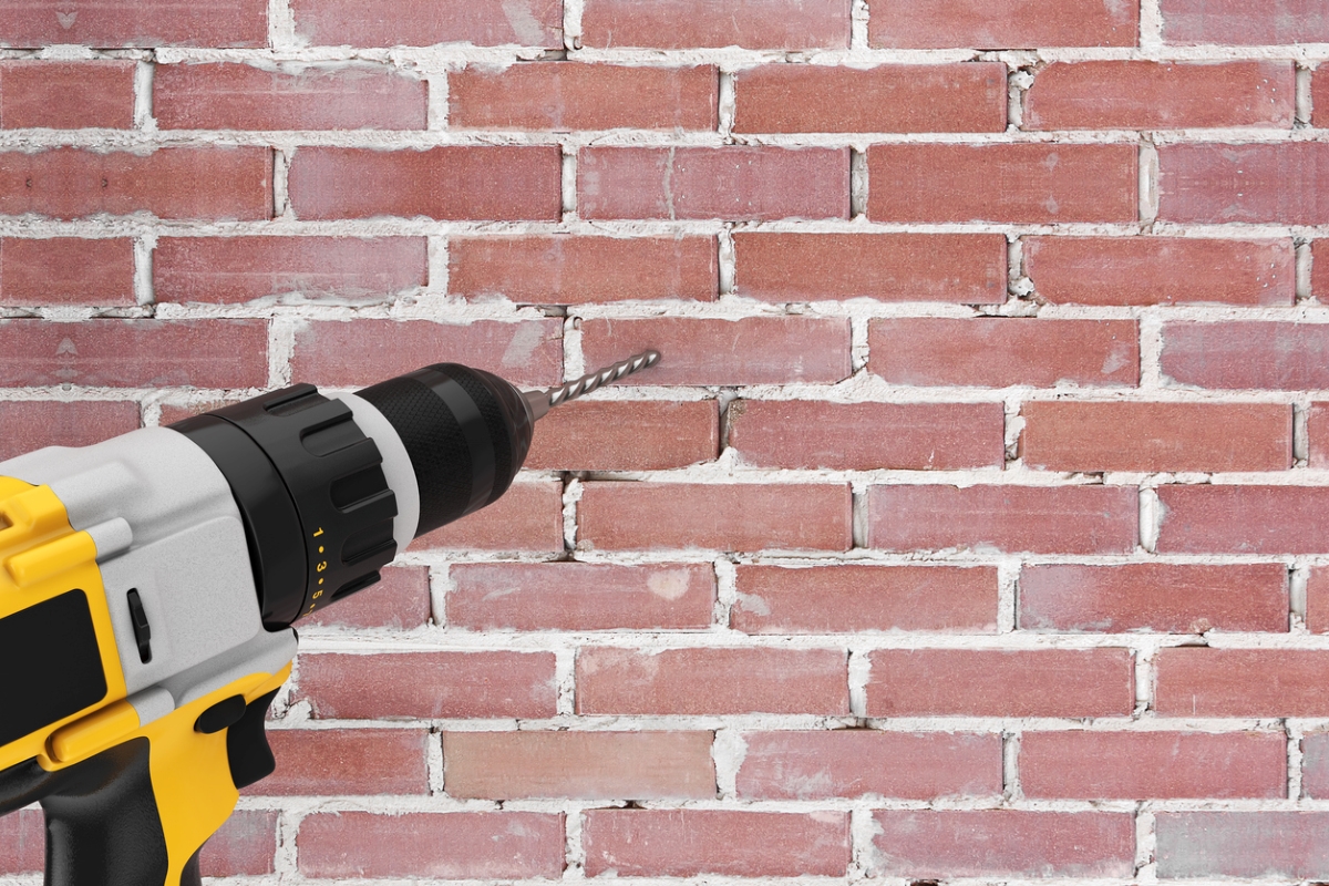 A yellow drill being used to drill hole into brick wall.