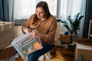 A woman transfers clothing from cardboard boxes to a plastic bin.