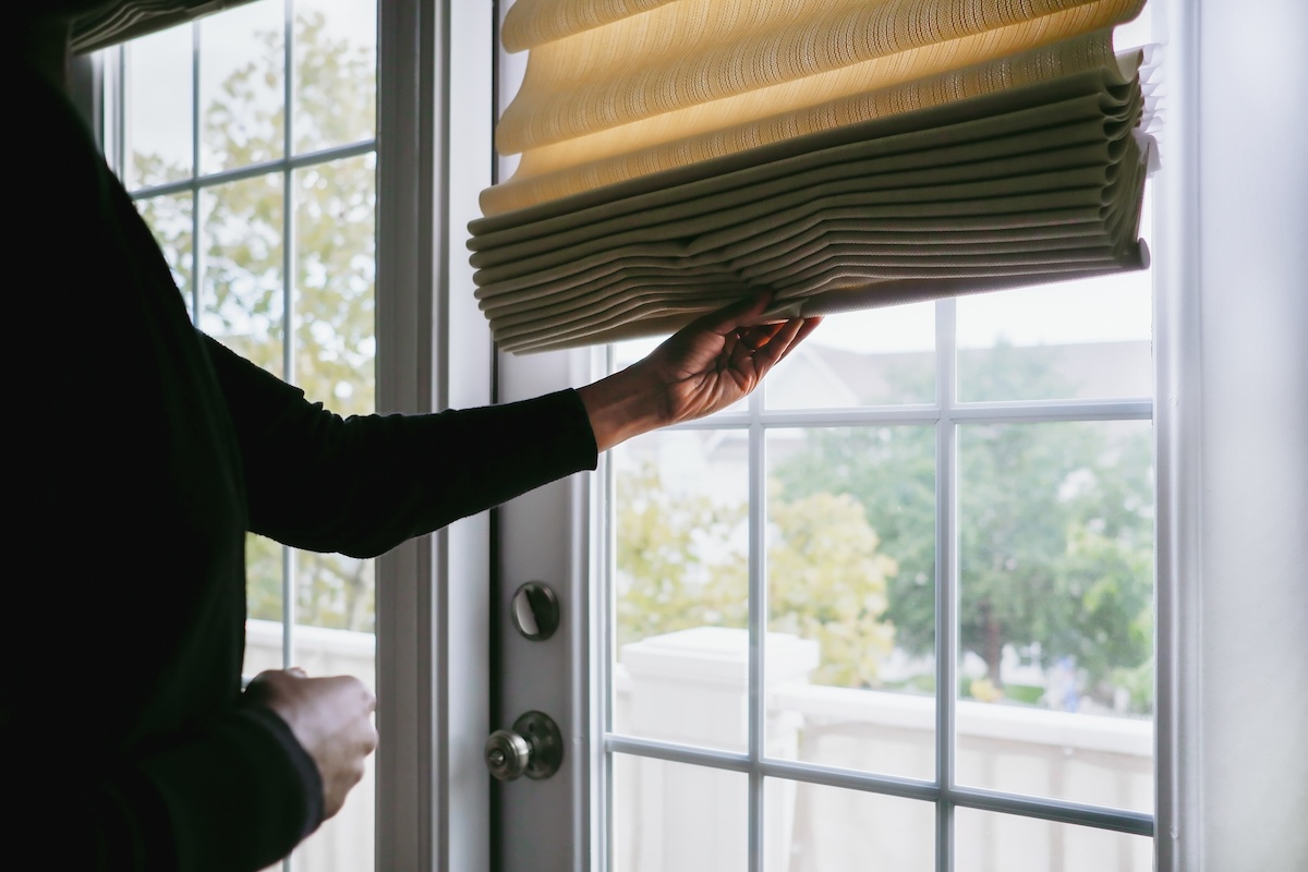 A woman pulls down the blind on a glass door.