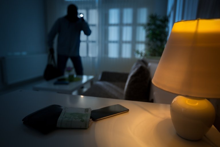 An intruder with a ski bask breaks into a dimly lit kitchen.