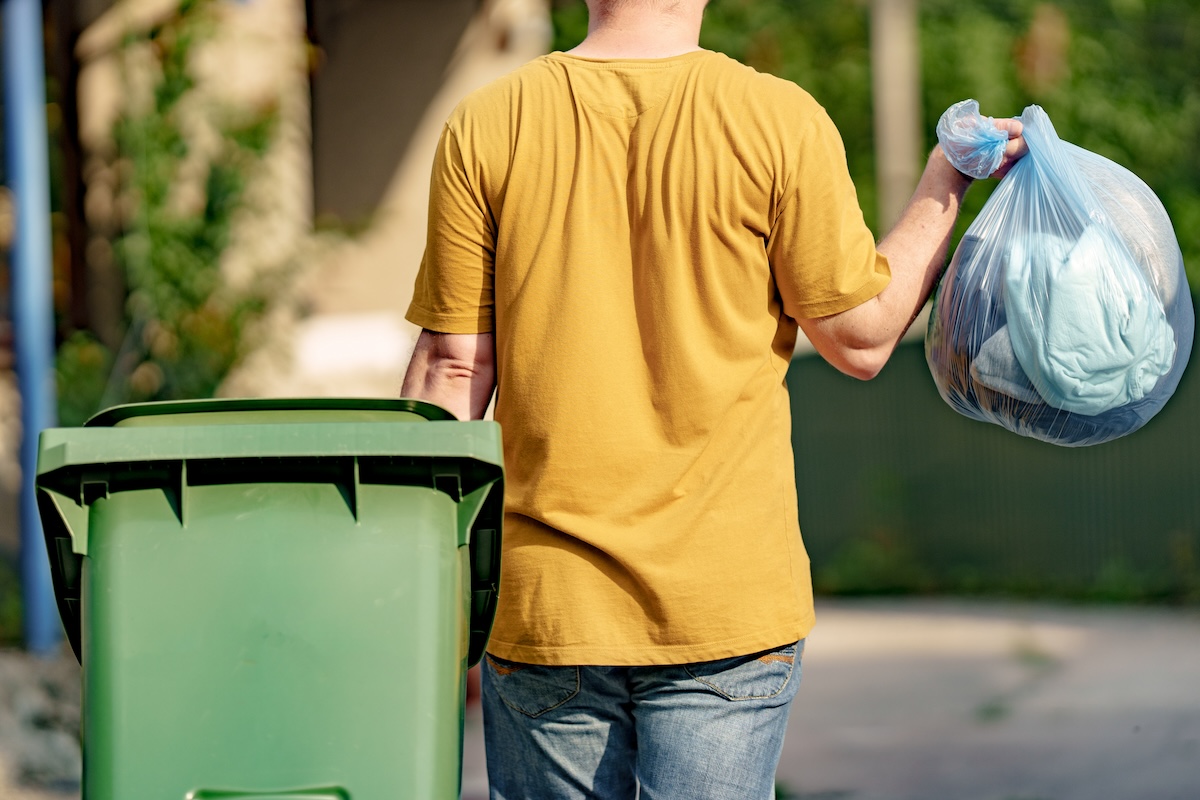 A man takes out a trash bad and trash bin.