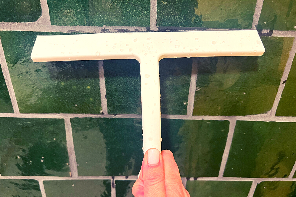 A person using the best shower squeegee to clean a green tile wall.