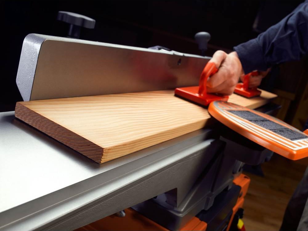 A person using the best jointer to smooth and flatten the face and edge of a piece of stock lumber.