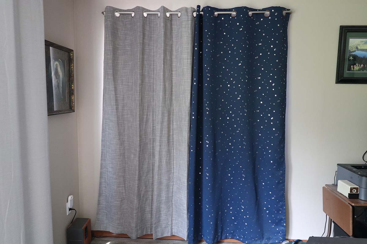 One grey thermal curtain and one star-patterned thermal curtain for kids installed over a patio door.