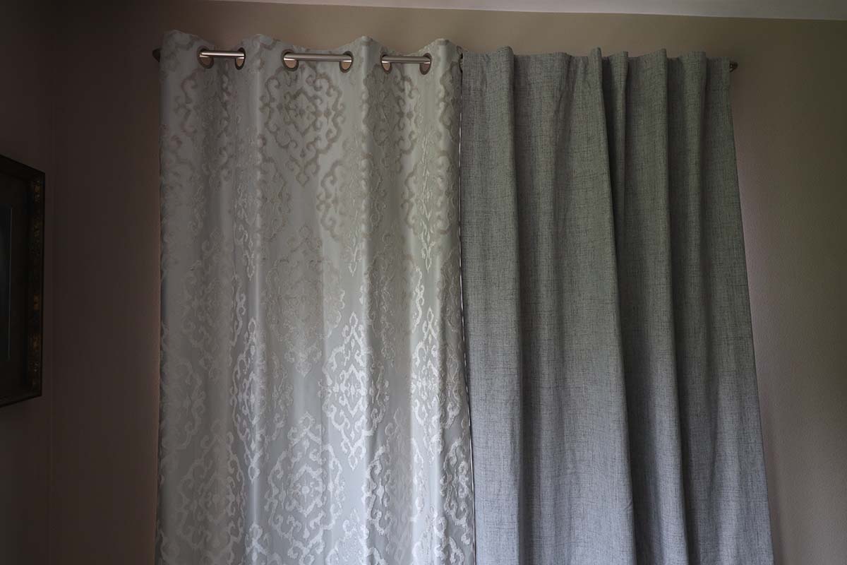 One patterned thermal curtain and one grey thermal curtain installed over a large window.