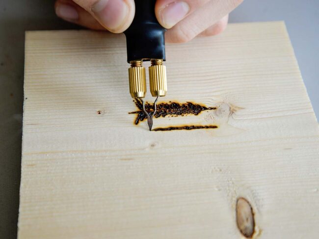 Person drawing two pine trees with a wood burning tool