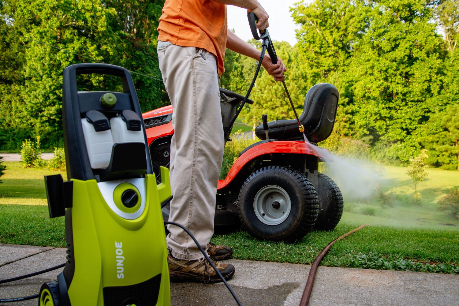 A person using the best electric pressure washer option to clean a riding lawn mower
