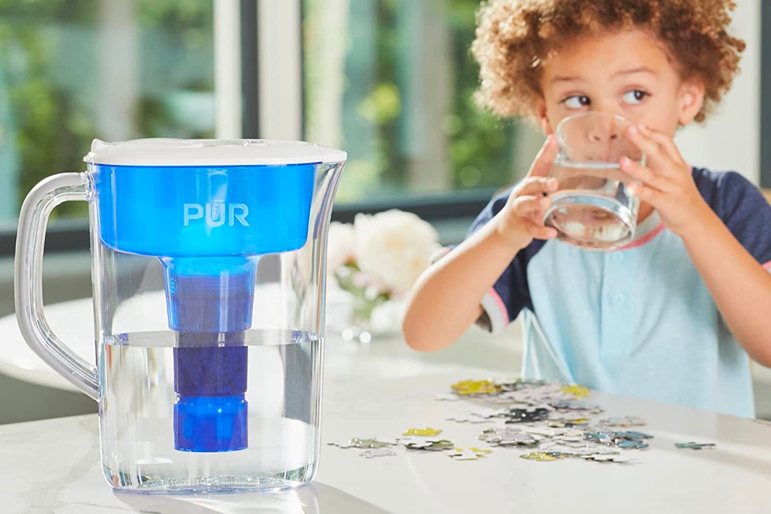 The best water filter pitcher option on a kitchen counter next to a young boy drinking a glass of water