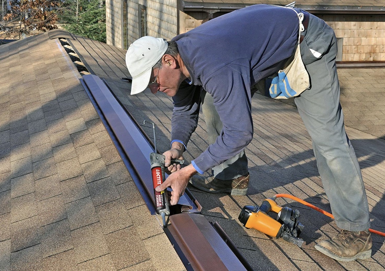Person putting Loctite roof and flashing sealant on the seam of a brown shingle